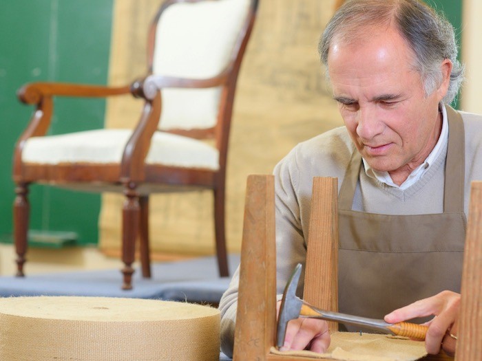 Man hammering upholstery on chair.